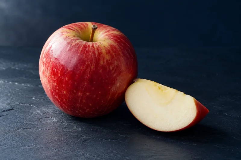 A red apple and a fresh apple wedge on a navy surface.