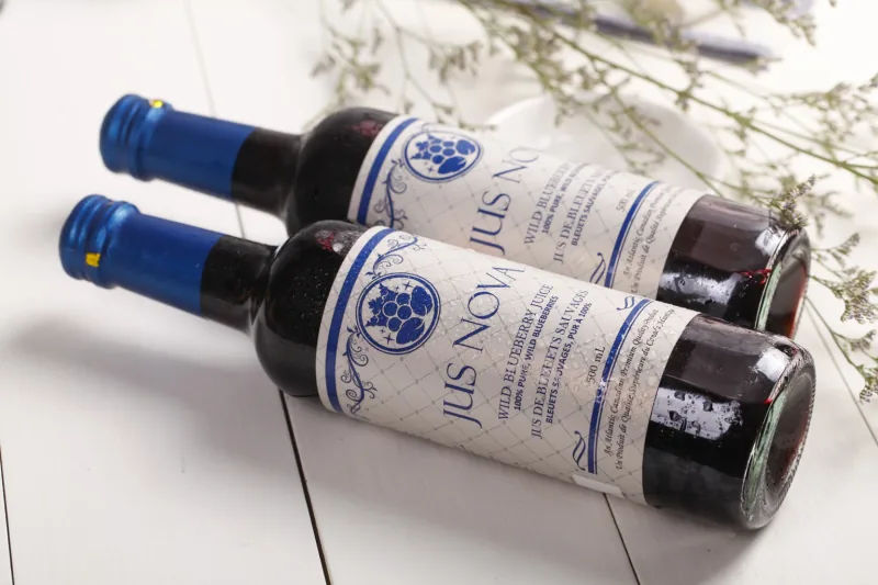 Two Jus Nova bottles reclining on a pale table.
