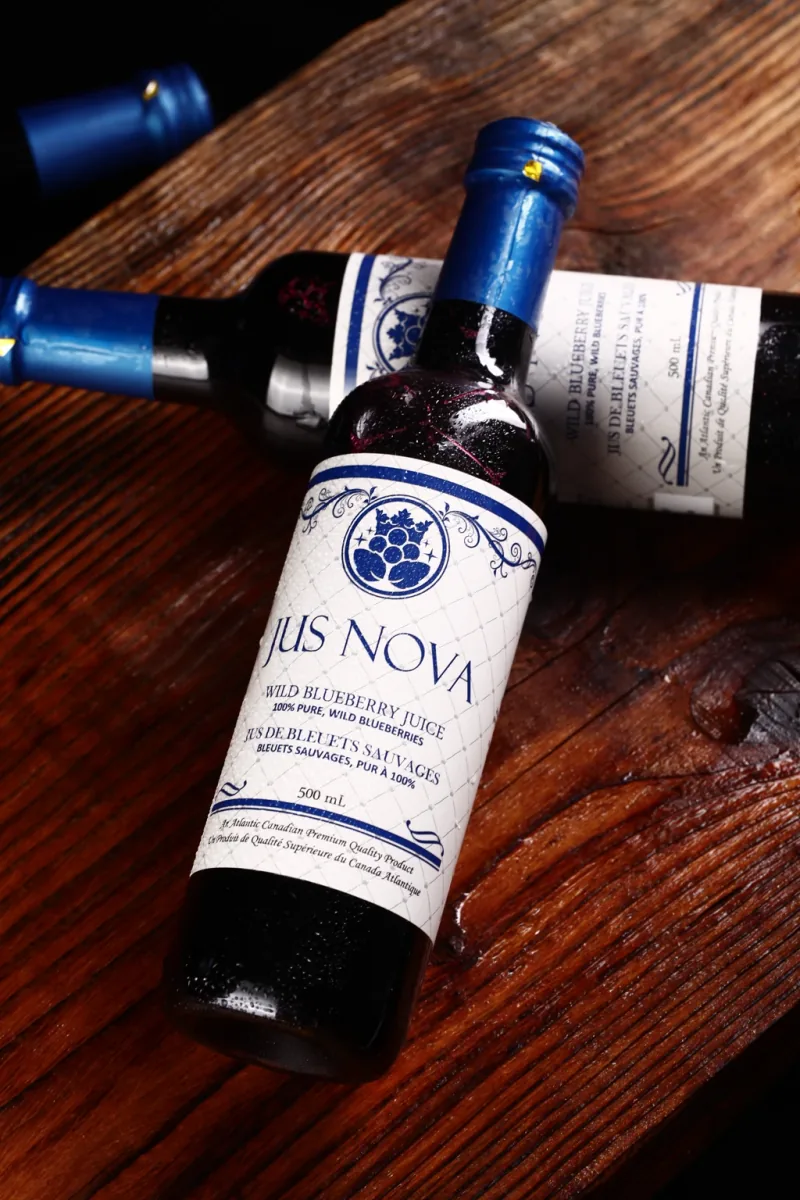 Two Jus Nova bottles crossed on dark wood.